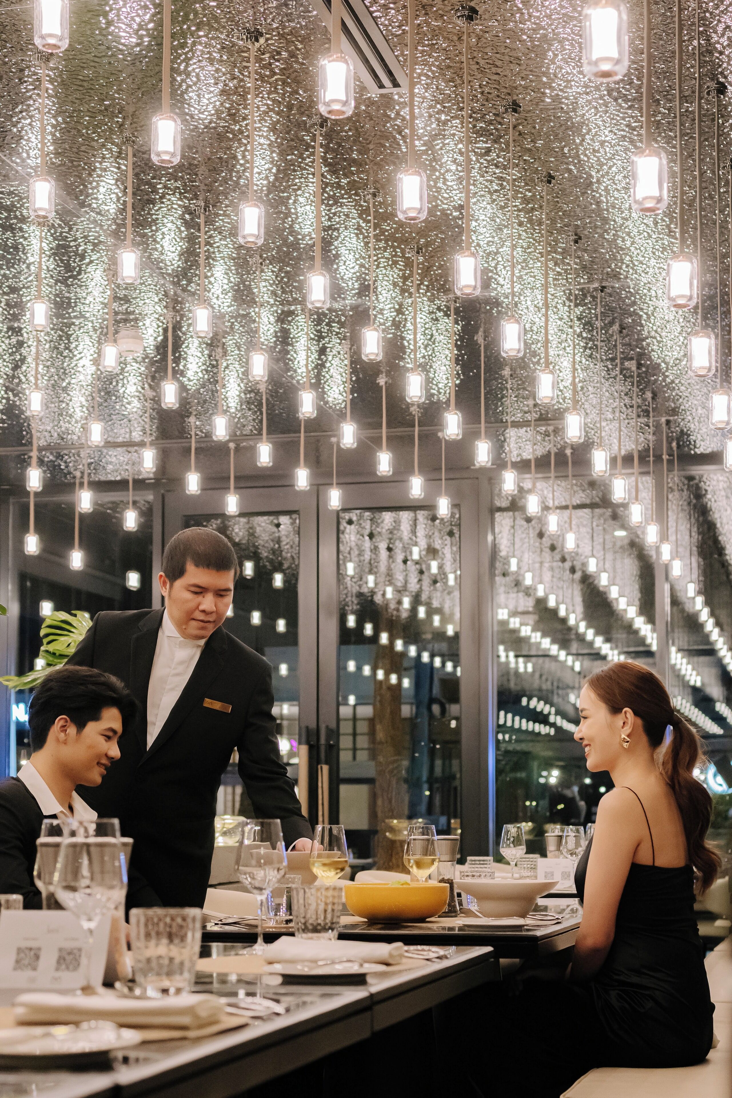 A formal dining setting with a waiter attending to guests, a table set with fine china, glasses, and a centerpiece.