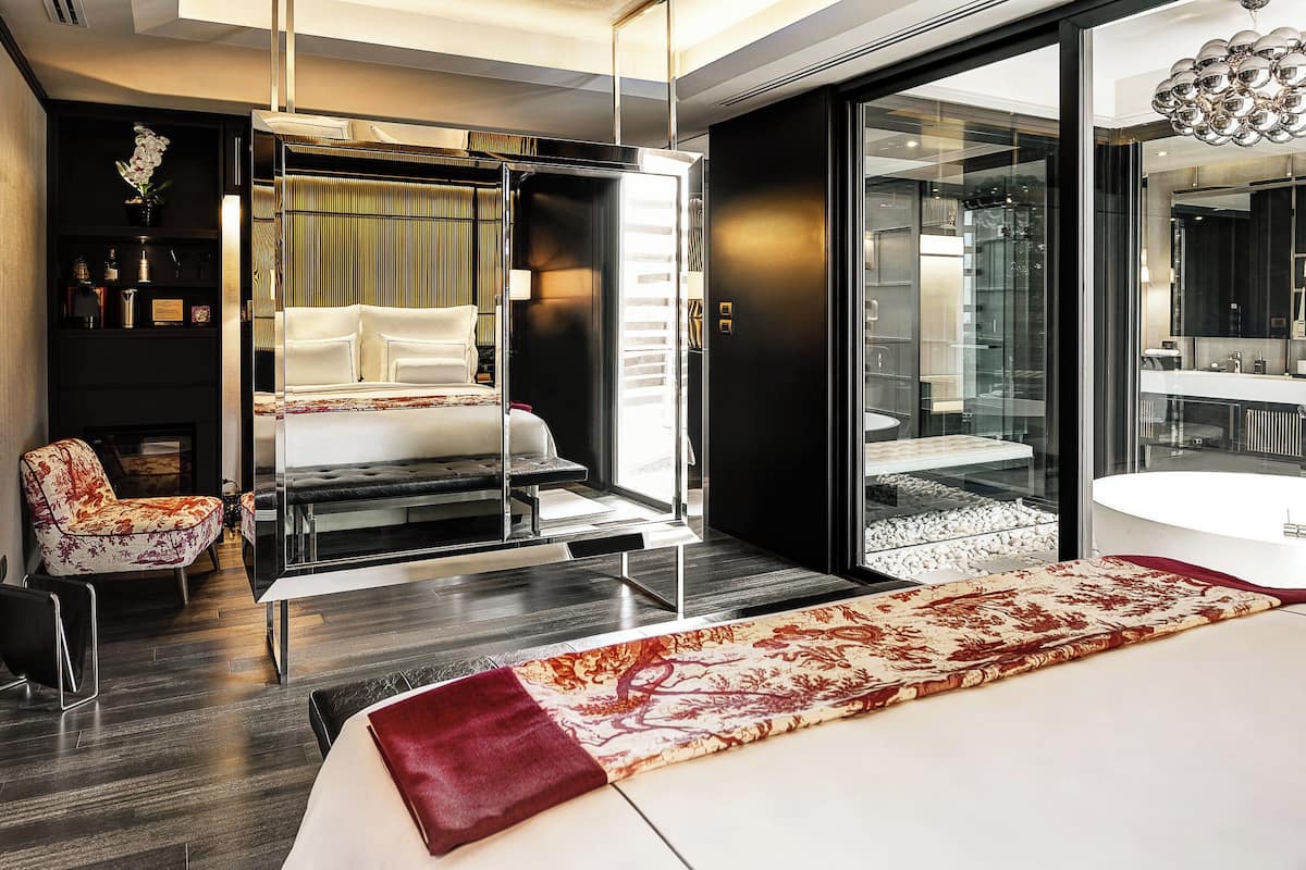 Ein modernes Hotelzimmer mit Bett, einer Couch, einer Glastrennwand und Blick auf eine Stadtlandschaft.