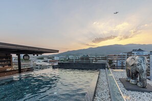 Uma piscina no terraço com vista para montanhas e um avião no céu.