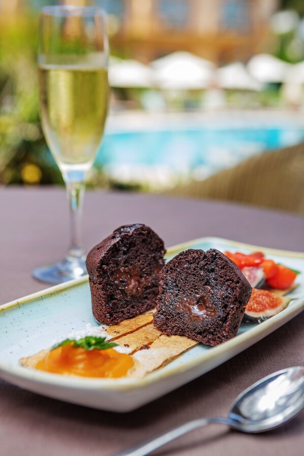 A dessert plate with chocolate lava cake, fruit, and a glass of white wine on a table.