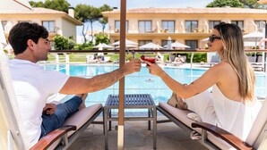Two people toasting with drinks by a poolside lounge chair, with a pool and a building in the background. - La Quinta Menorca by Portblue Boutique (Ciutadella de Menorca)