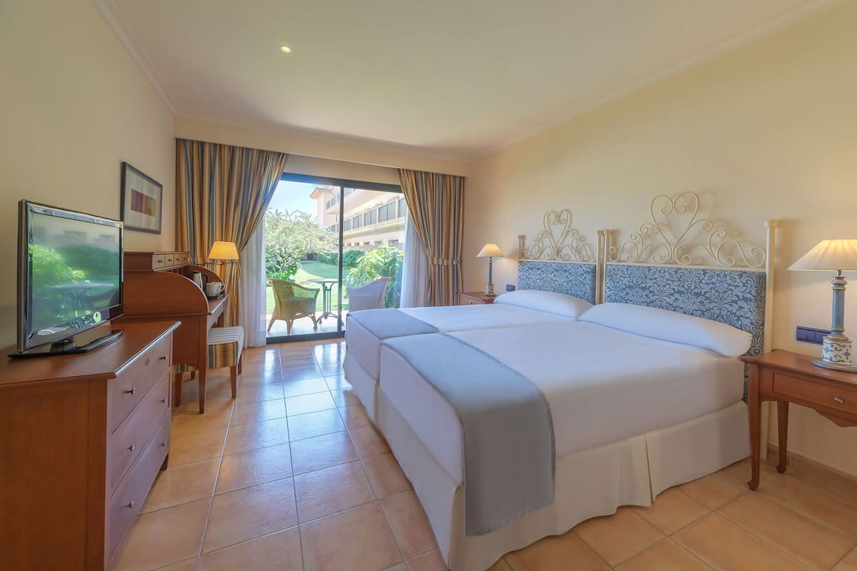 Quarto de hotel com uma cama, uma escrivaninha com televisão, uma cadeira, uma mesa e vista para o exterior.