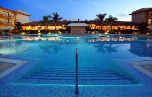 A large, clear swimming pool with a central pole, surrounded by palm trees and a building with multiple balconies. - La Quinta Menorca by Portblue Boutique (Ciutadella de Menorca)