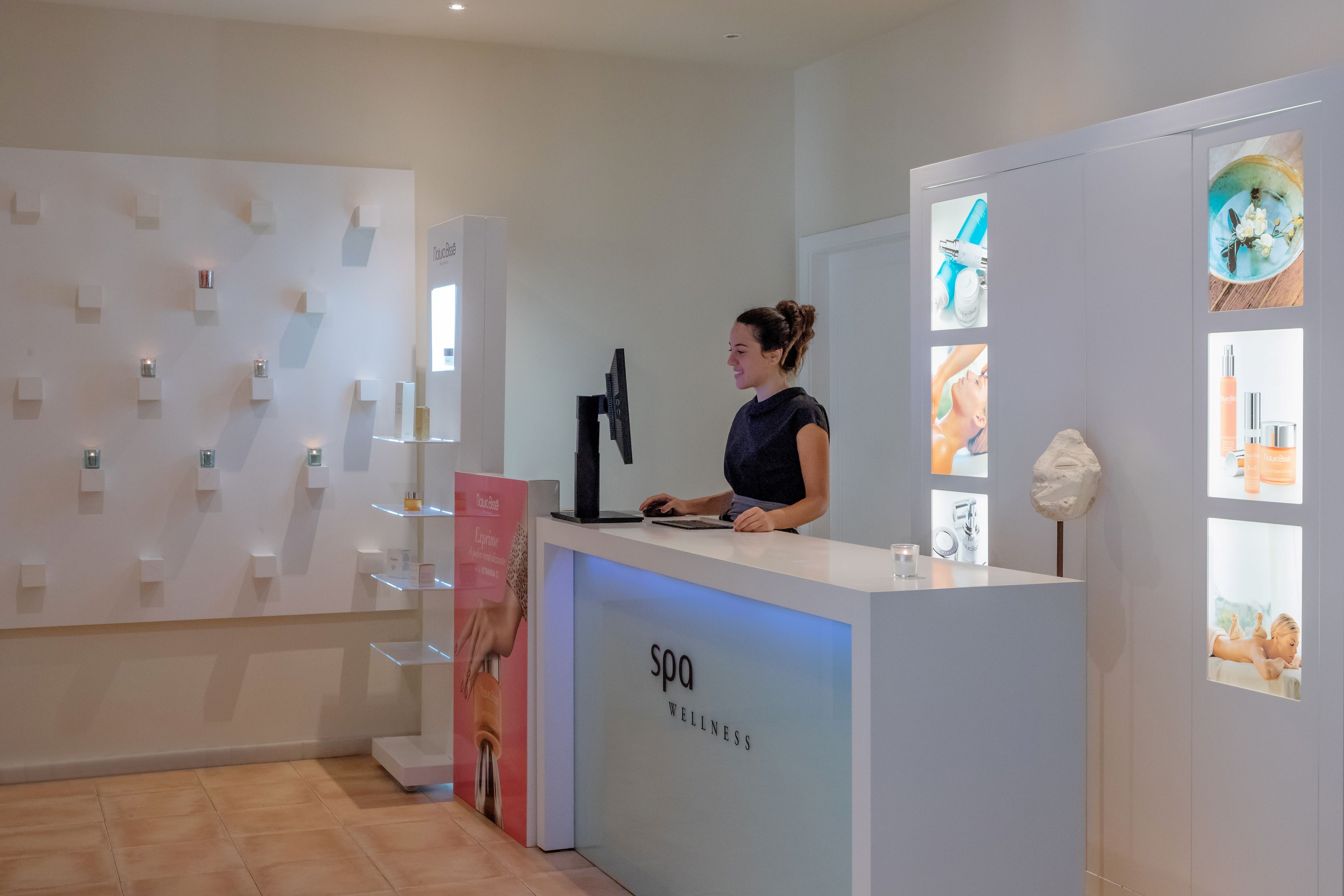 Een receptiebalie van een wellnesscentrum met een modern design, een computer en een digitaal scherm.