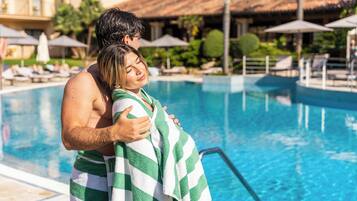 A couple embracing by a pool with lounge chairs and umbrellas in the background.