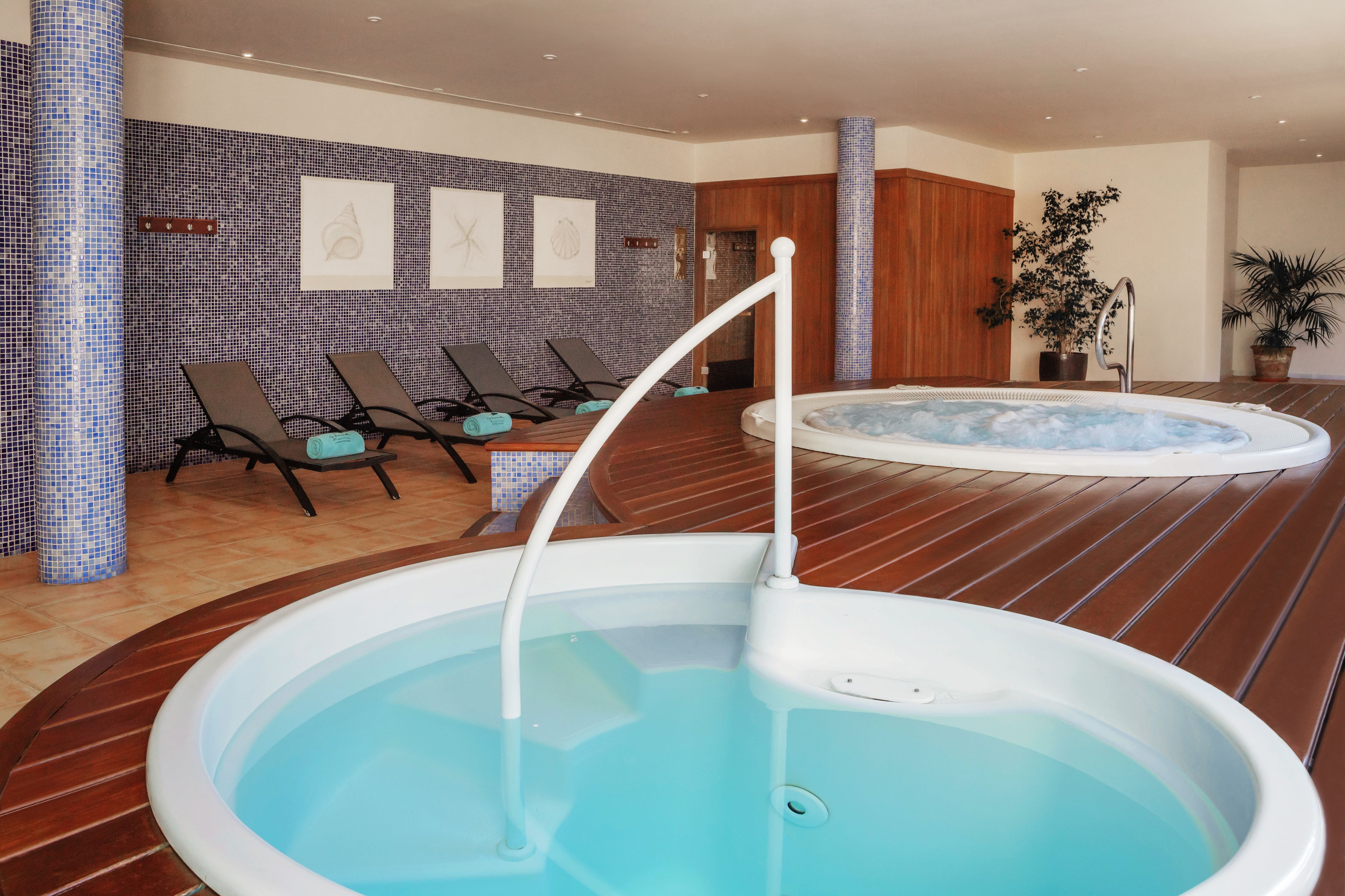 A spa area with a hot tub, lounge chairs, and a tiled wall with artwork.