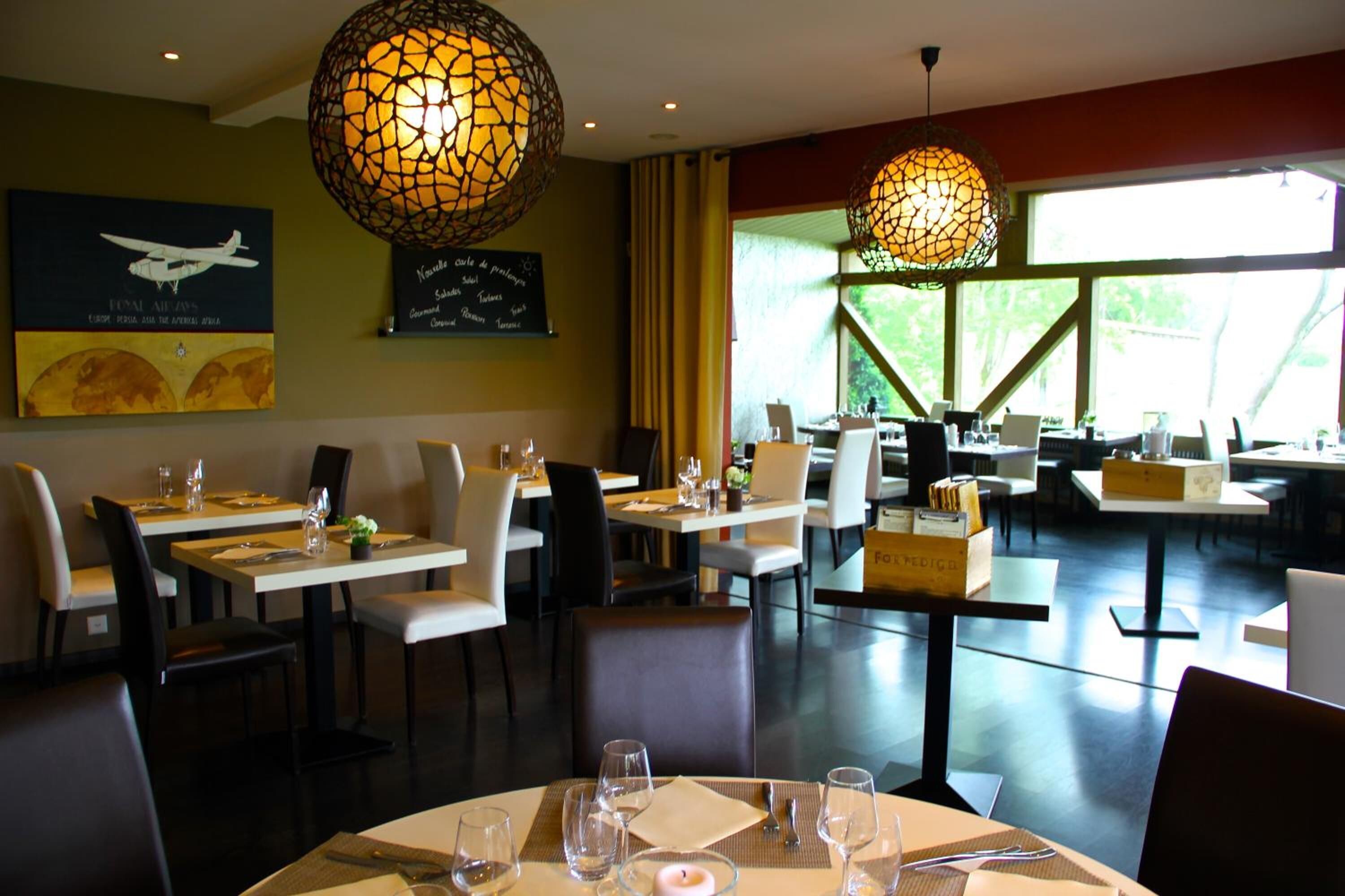 Een restaurant met ronde tafels, stoelen en hangende bolvormige lampen.