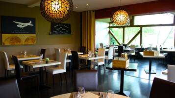 Een restaurant met ronde tafels, stoelen en hangende bolvormige lampen.