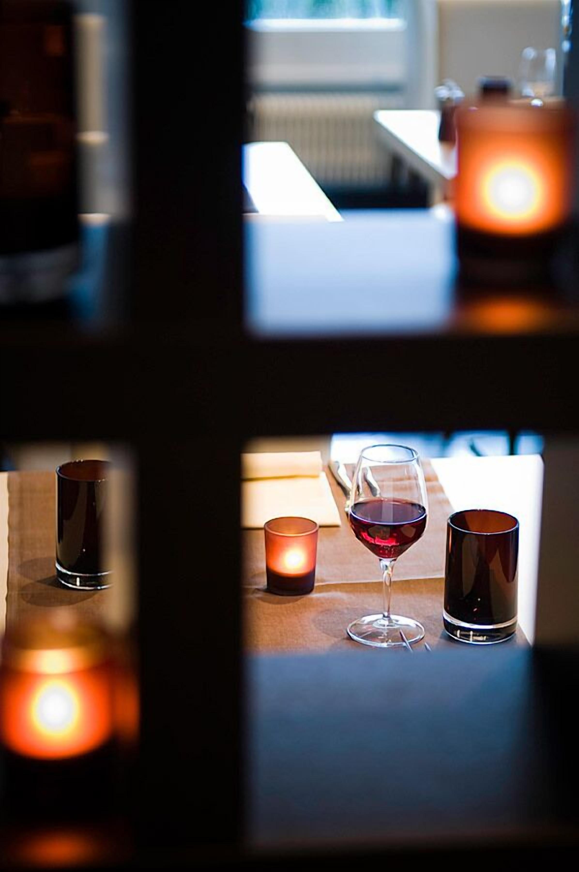 Ein schummriges Zimmer mit einem Tisch, auf dem eine Kerze, ein Glas Rotwein und ein Kerzenhalter stehen.
