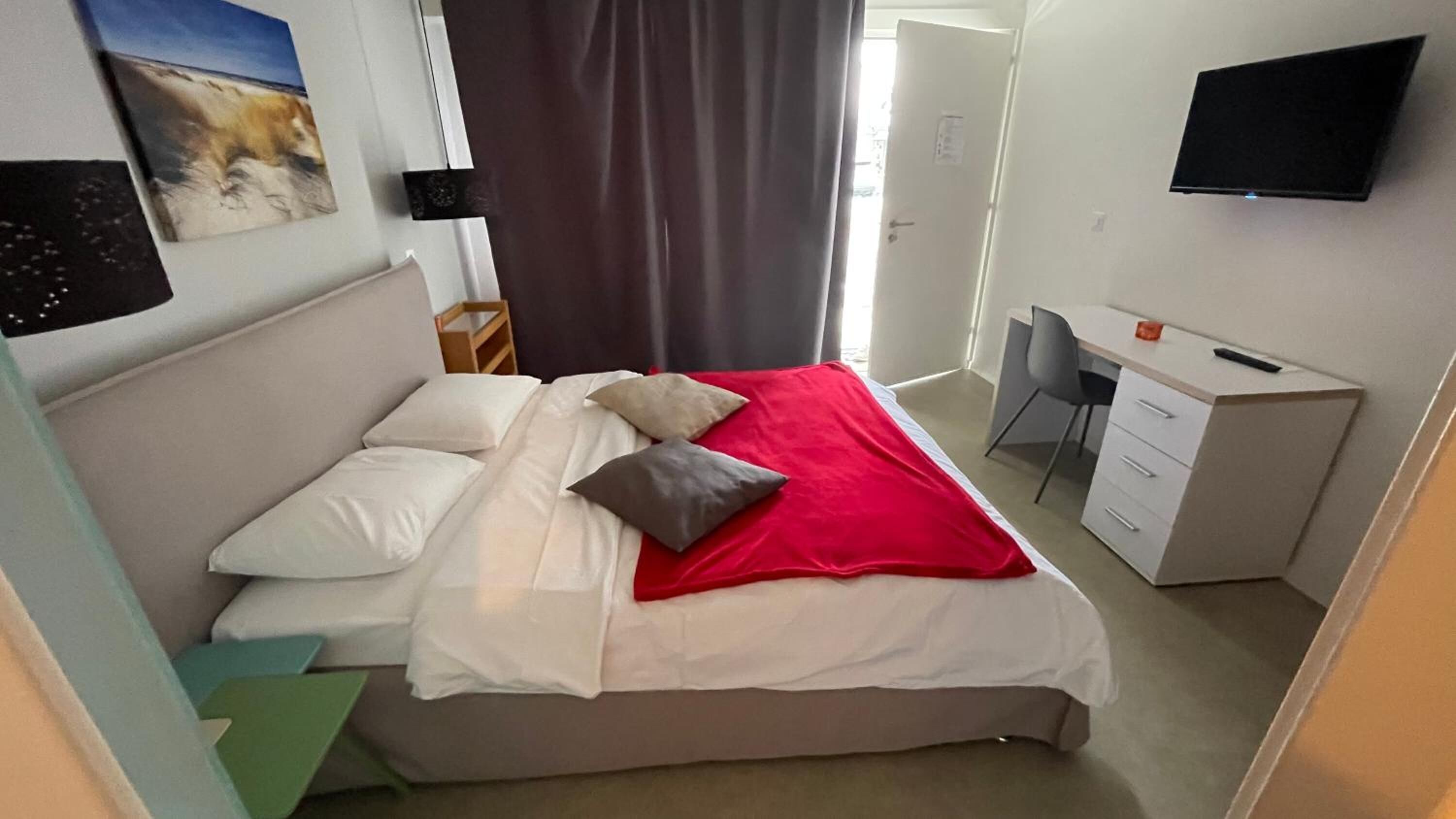 A hotel room with a bed, a desk, a chair, and a TV on the wall.