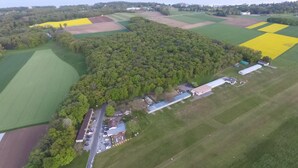 Luchtbeeld van een landelijk gelegen pand met velden, een bebost gebied en een klein gebouwendom, met een weg er naartoe.