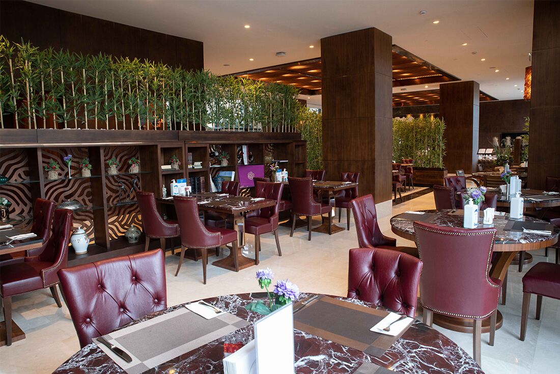 Un restaurante moderno con techos altos, paneles de madera oscura y sillas de cuero rojo.