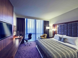 Una habitación de hotel con una cama grande, un escritorio con una silla, un televisor y una ventana con cortinas.