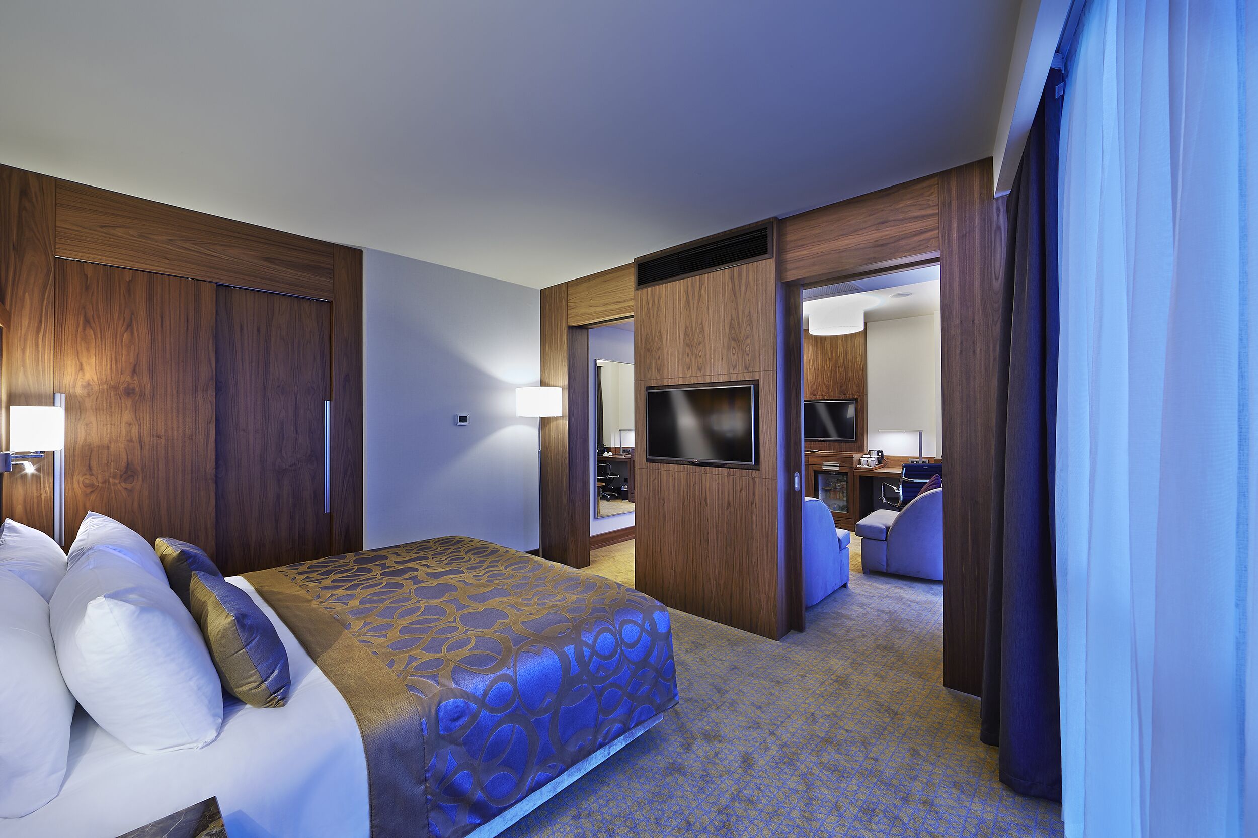 A hotel room with a bed, a TV, and a bathroom visible through an open door.