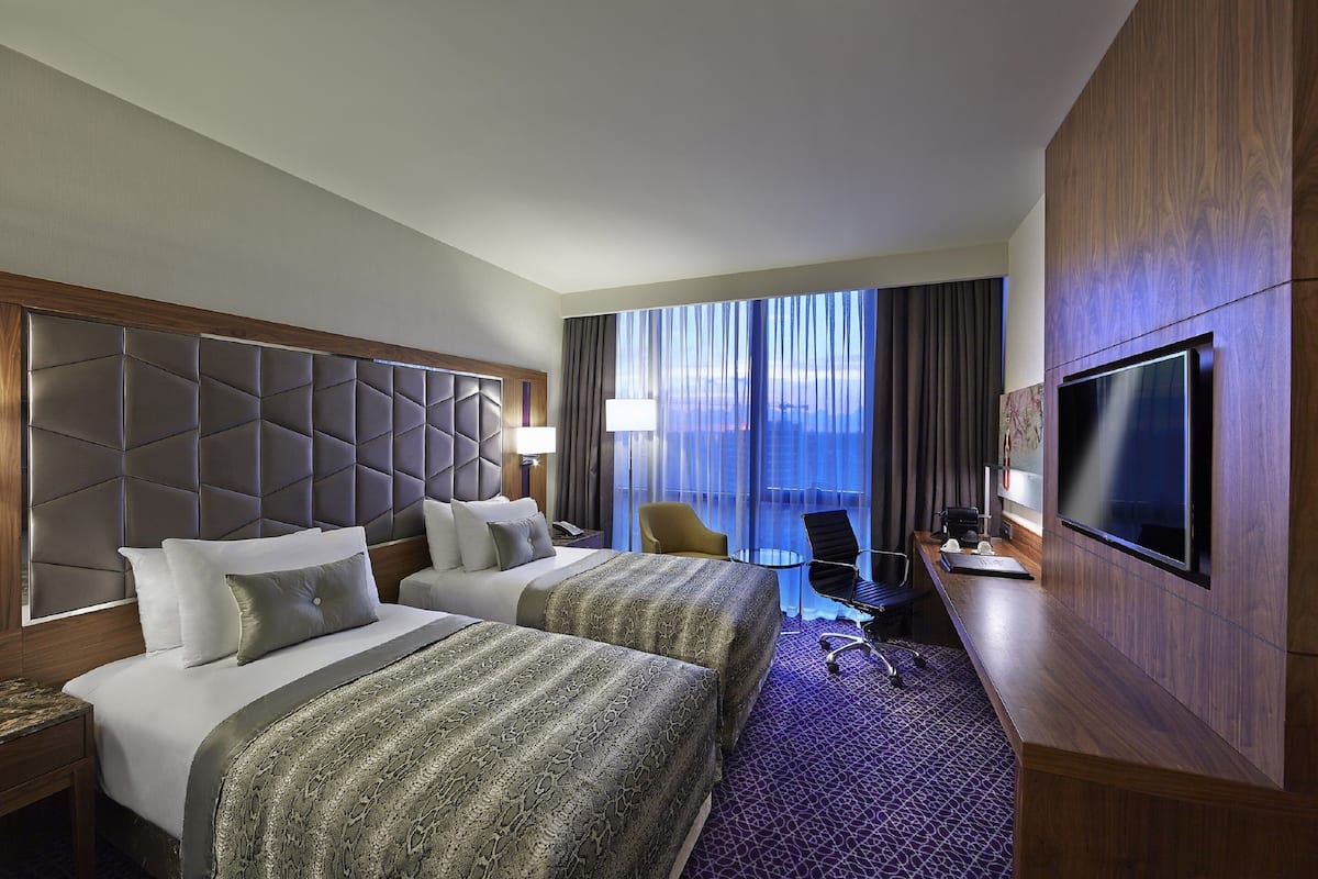 Habitació d'hotel amb dos llits, un escriptori, televisió i vista a la ciutat.
