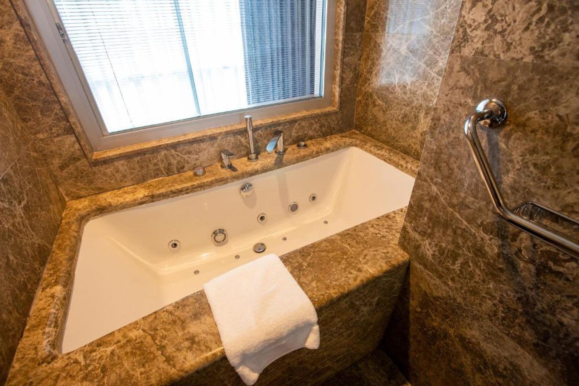 A bathroom with a marble sink, a bathtub, and a window with blinds.