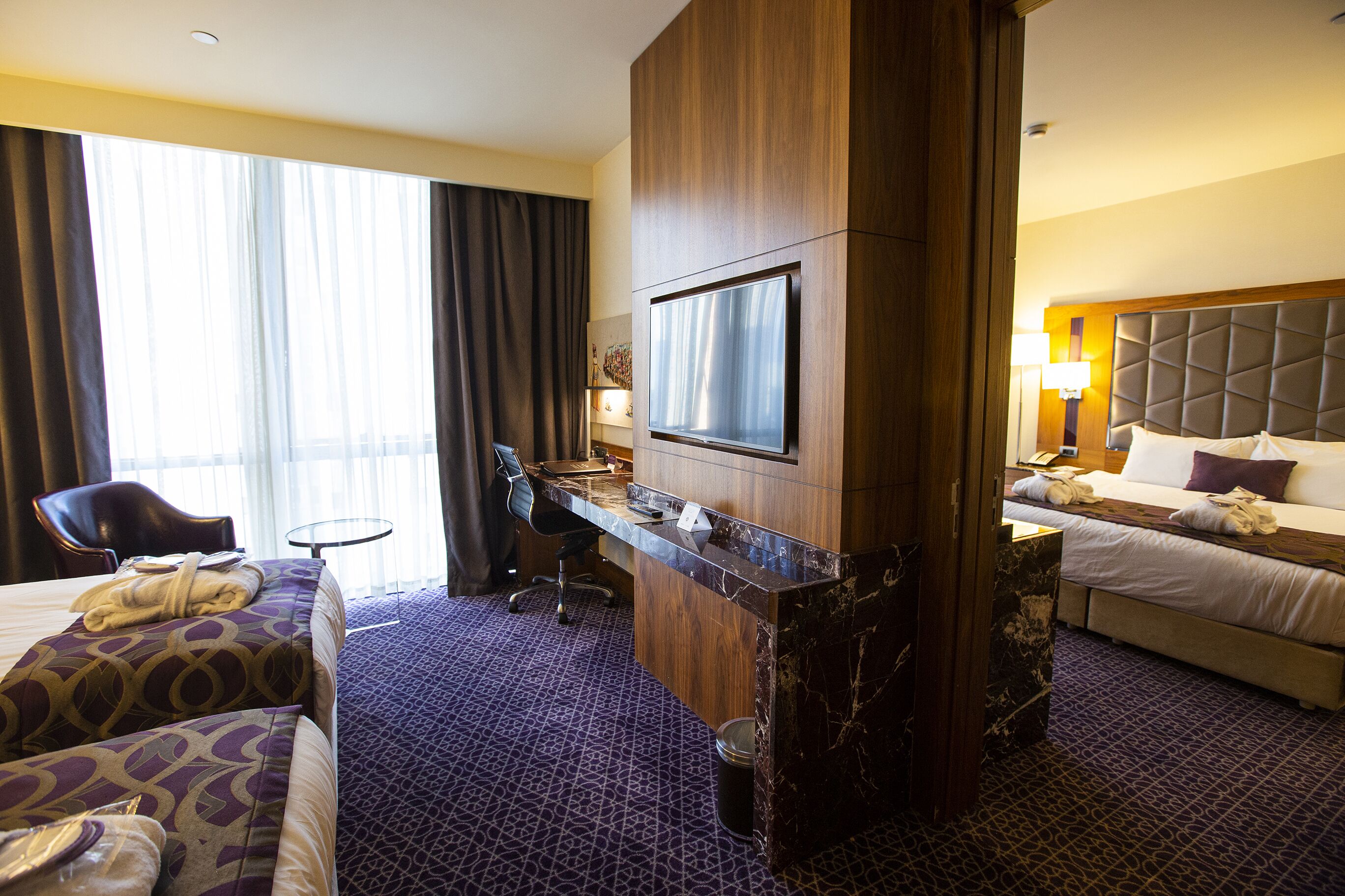 A hotel room with a bed, a desk, a chair, a television, and a large window with curtains.