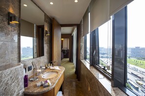 A modern bathroom with a large sink, mirror, and a view of the city through large windows.