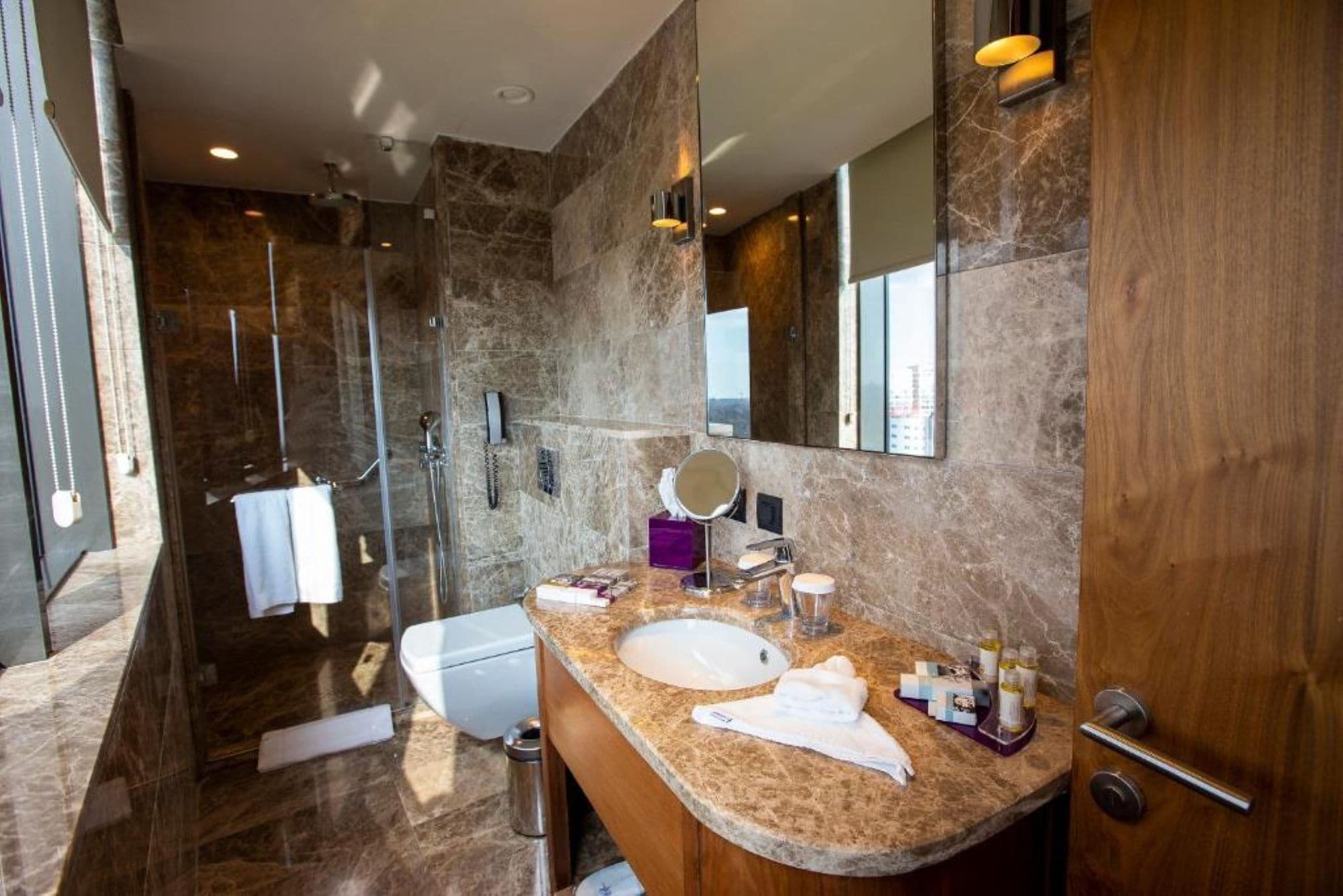 Un baño moderno con lavamanos de mármol, ducha con mampara de vidrio y un espejo grande.