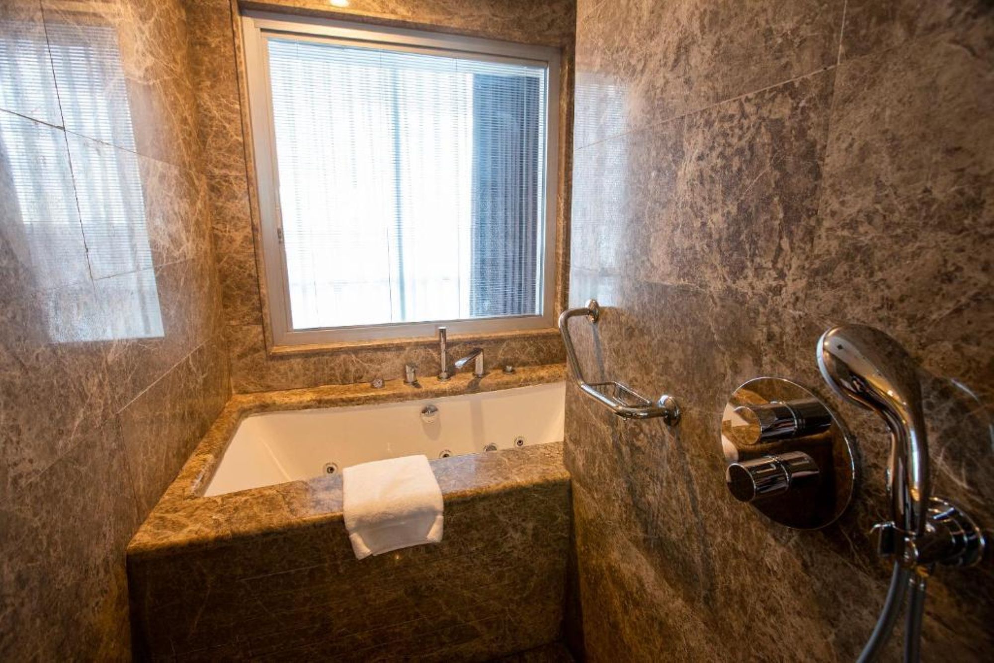A bathroom with a marble sink, a window with blinds, and a shower area.