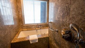 A bathroom with a marble sink, a window with blinds, and a shower area.