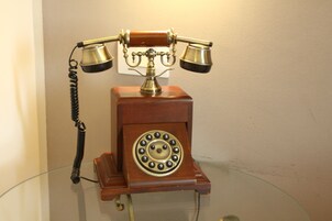 Un teléfono antiguo de disco giratorio sobre una mesa de vidrio frente a una pared lisa.