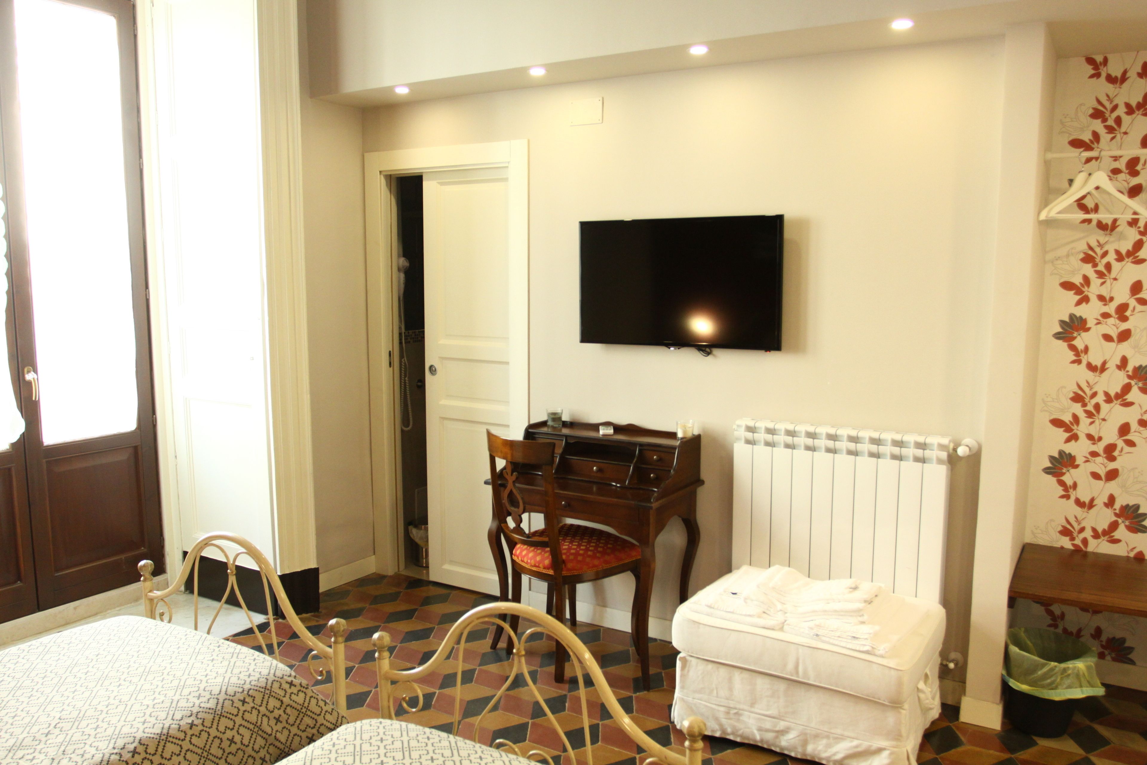 A room with a bed, a desk, a chair, a radiator, and a television on the wall.