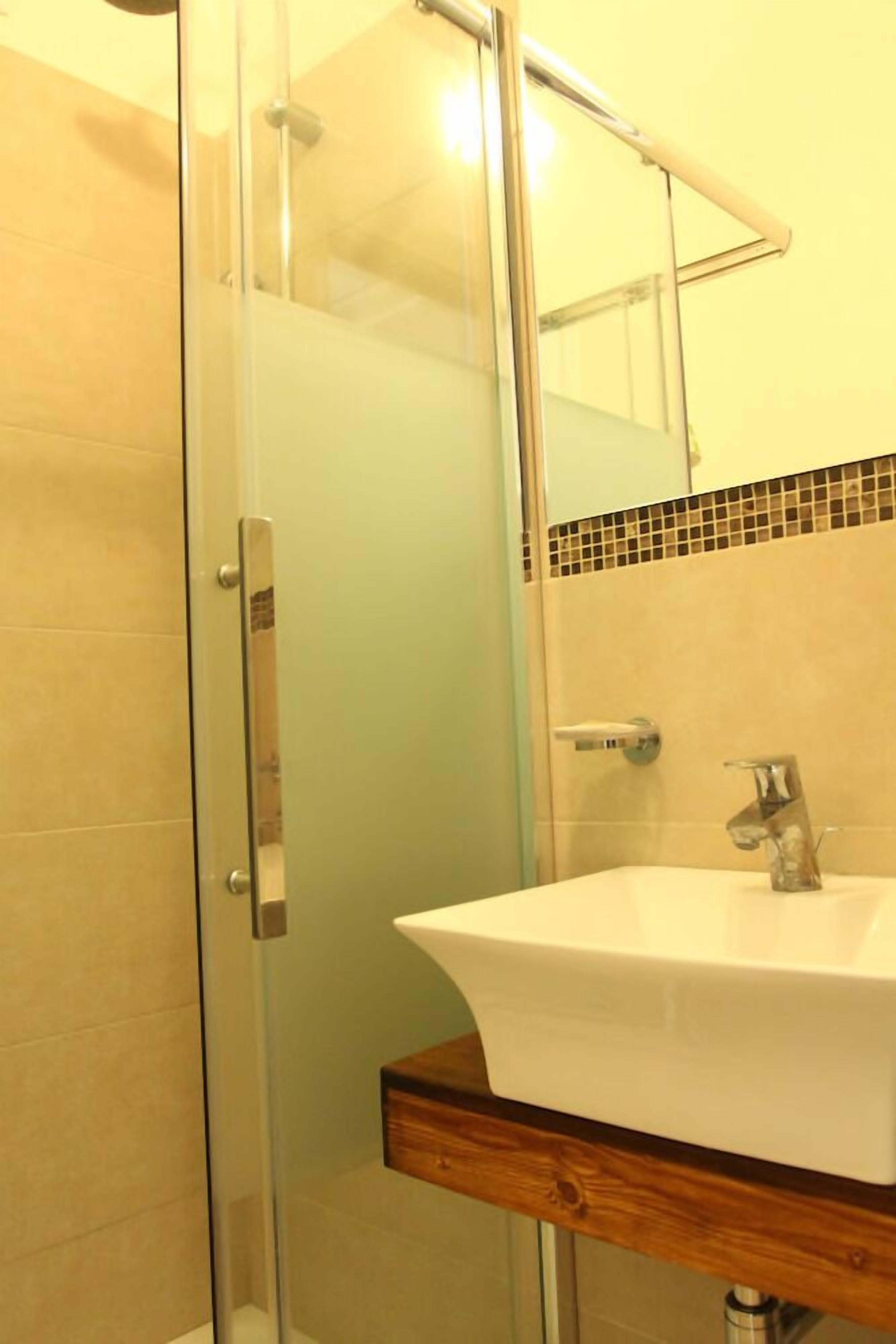 A bathroom with a glass shower enclosure, a white sink, and a wooden countertop.