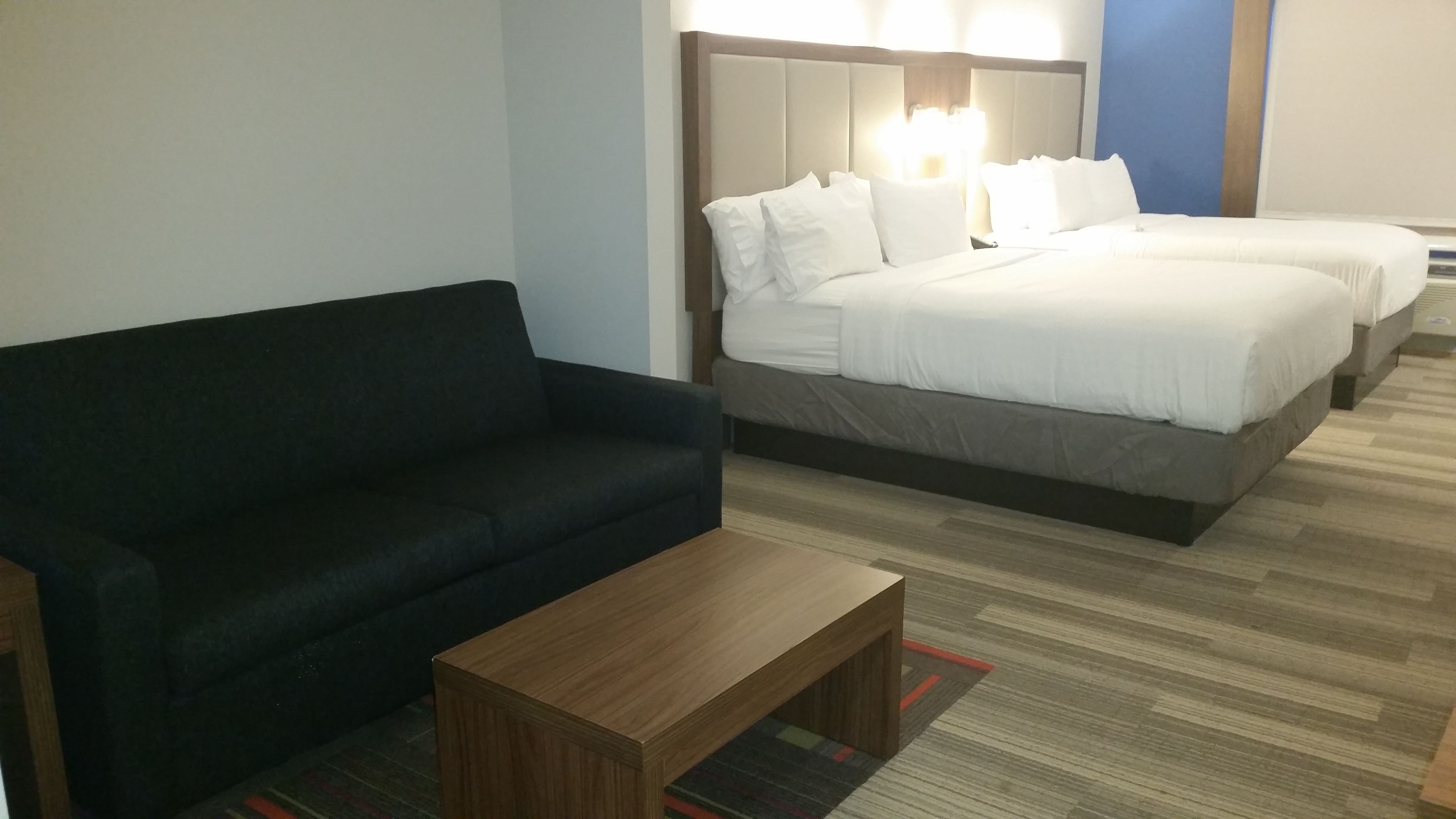Ein Hotelzimmer mit einem dunkelgrauen Sofa, einem Holztisch und einem Bett mit weißer Bettwäsche.