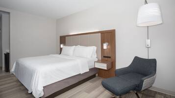 A modern hotel room with a large bed, a nightstand, a chair, and a wall-mounted lamp.
