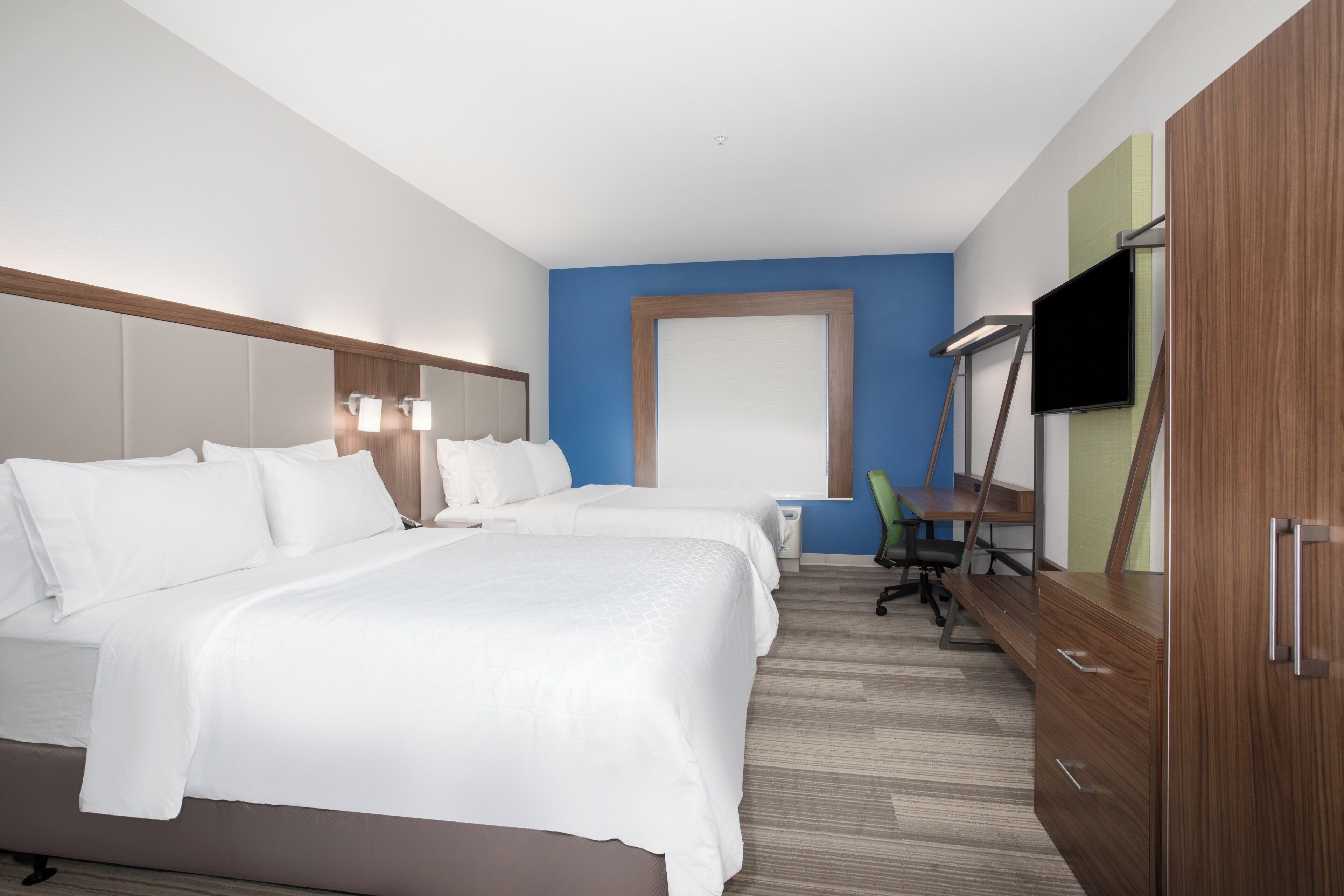A hotel room with a large bed, a desk, a chair, and a television.