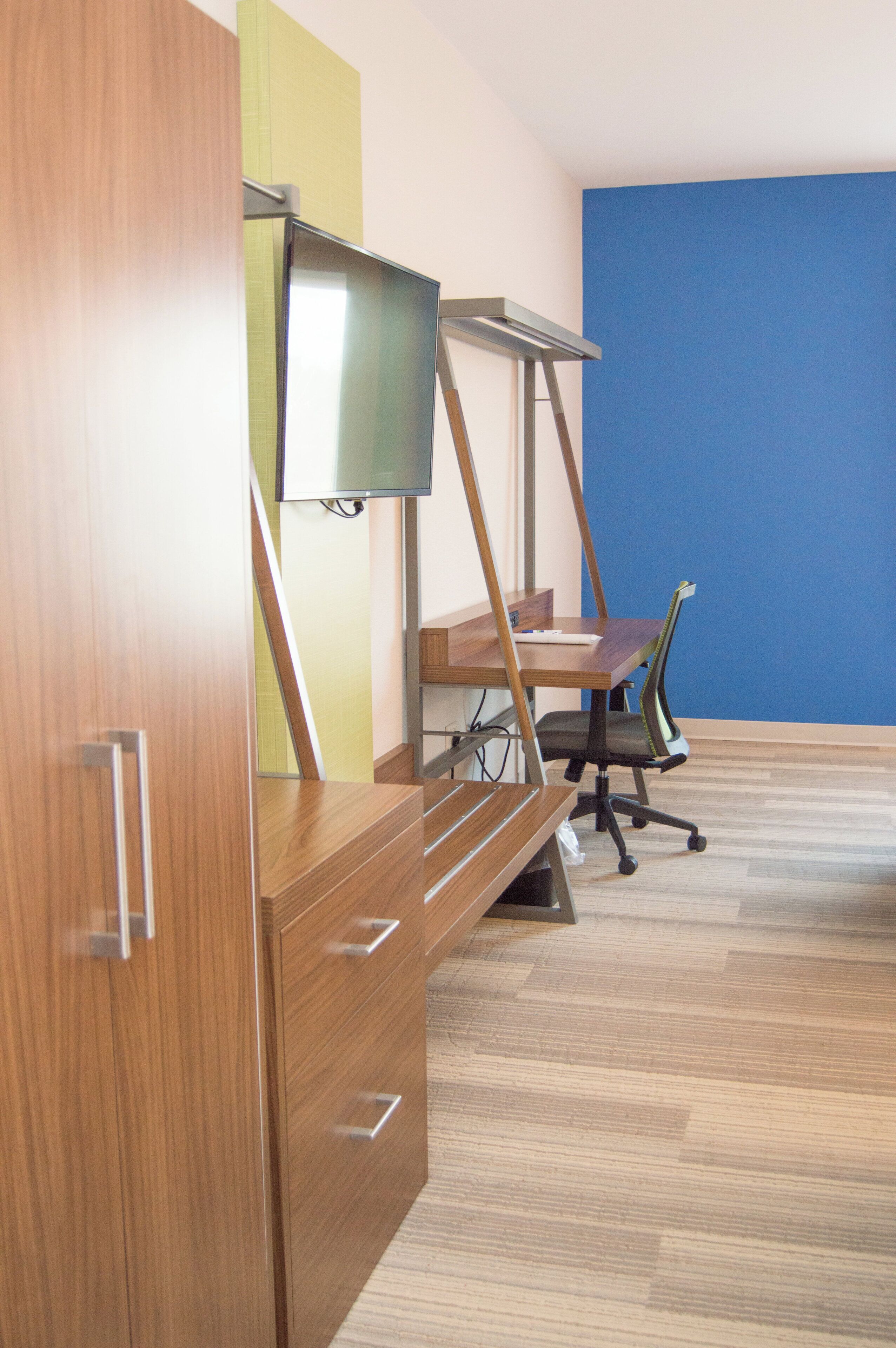 A room with a wooden desk, a chair, a television on a stand, and a blue wall.