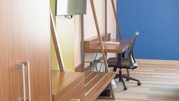 A room with a wooden desk, a chair, a television on a stand, and a blue wall.