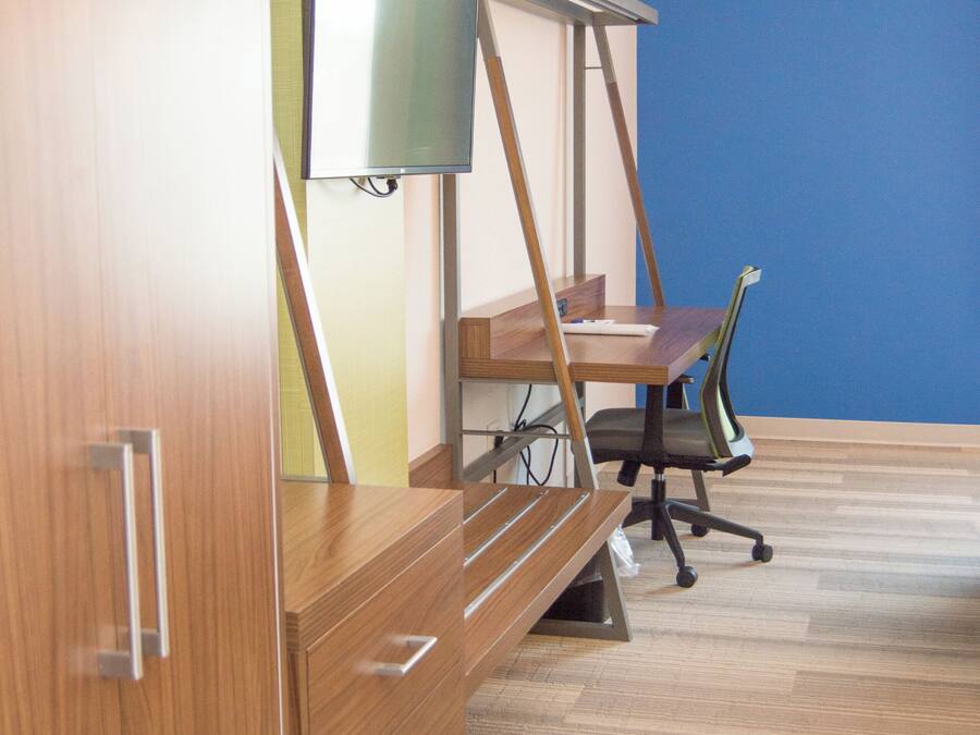 A room with a wooden desk, a chair, a television on a stand, and a blue wall.