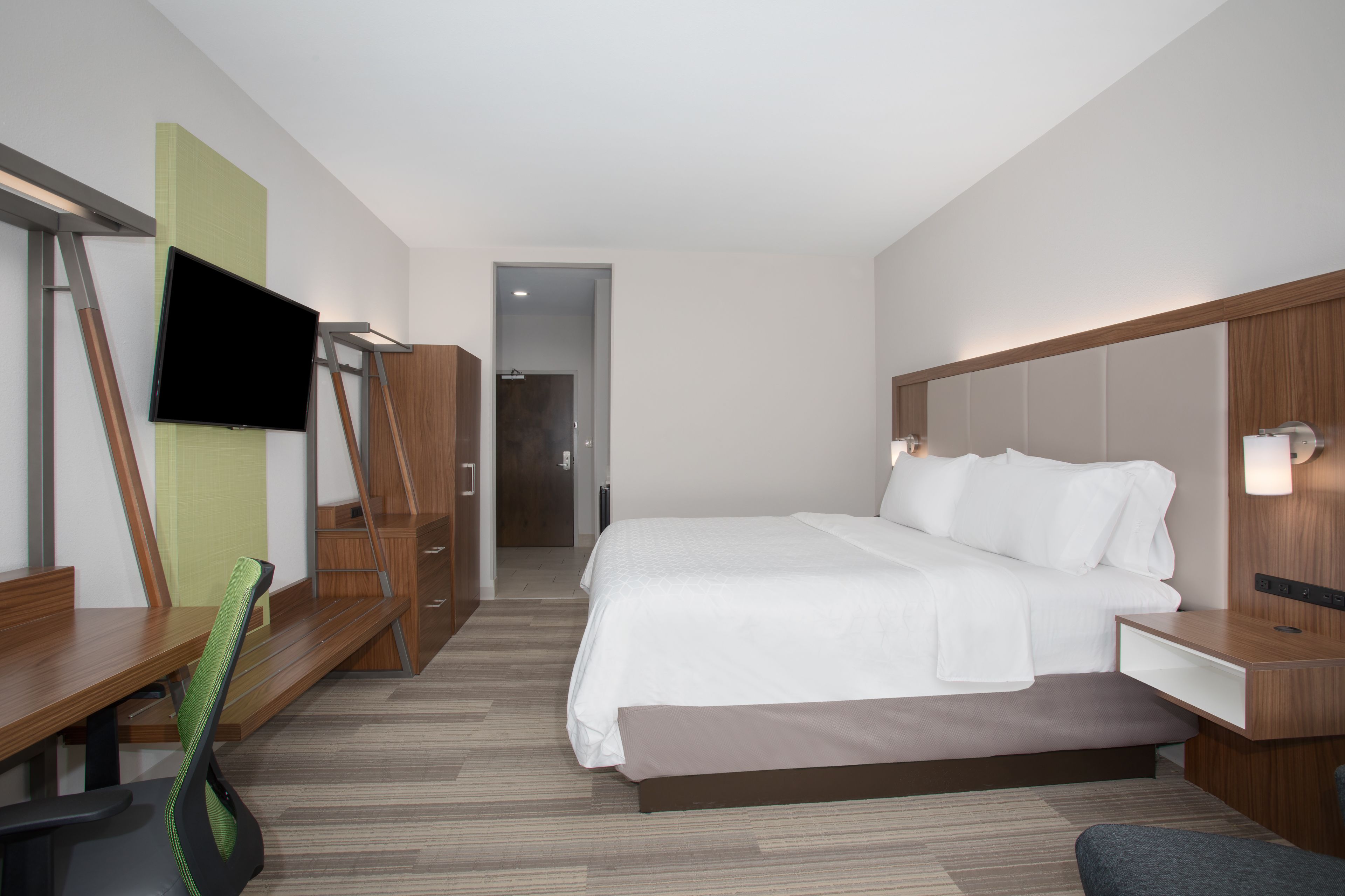 Une chambre d’hôtel moderne équipée d’un grand lit, d’un bureau, d’une chaise, d’une télévision et d’une armoire.