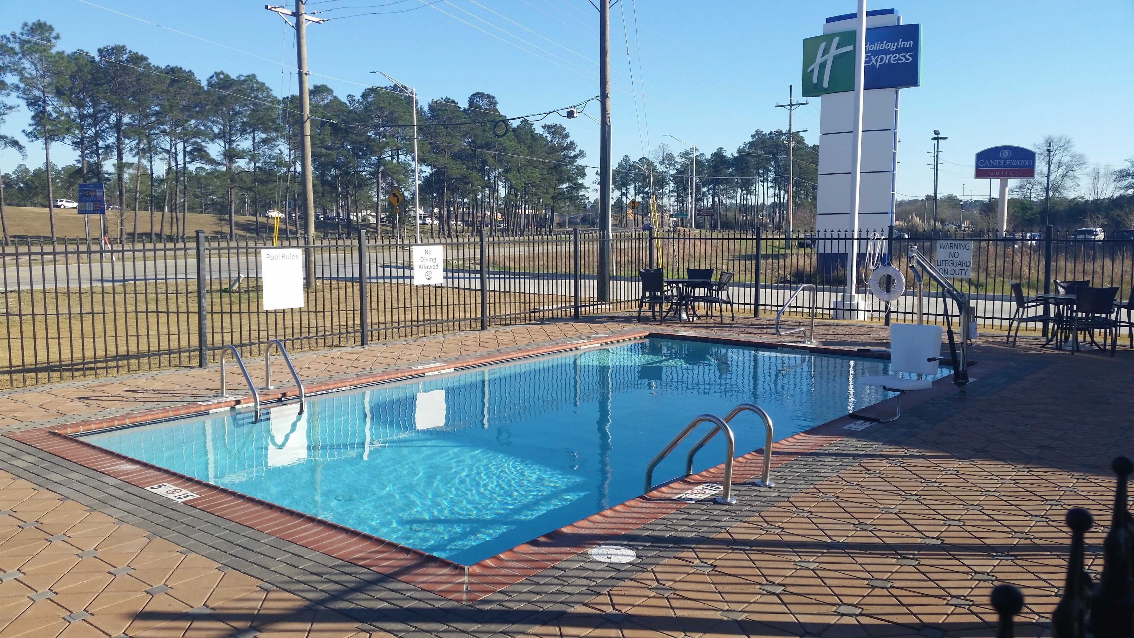 A swimming pool with a fenced area, pool rules sign, and a lifeguard duty sign.