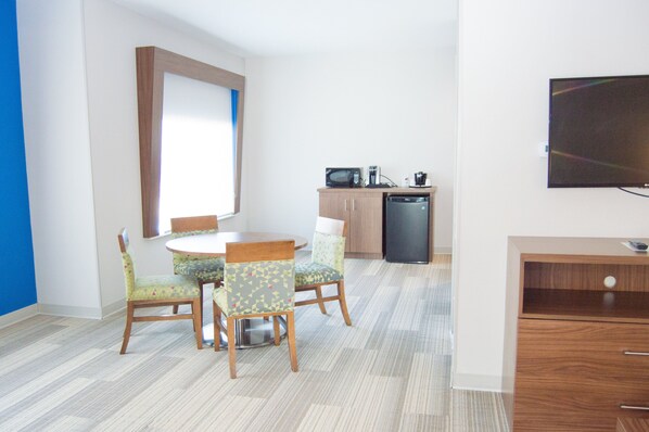 A compact room with a dining table, chairs, a microwave, a coffee maker, and a TV.