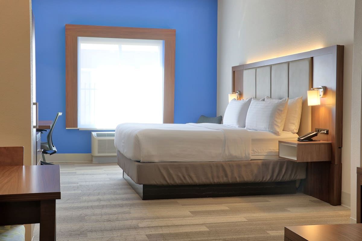 Moderni hotellihuone, jossa on suuri sänky, yöpöytävalaisimet ja ikkuna, jossa on sälekaihtimet.