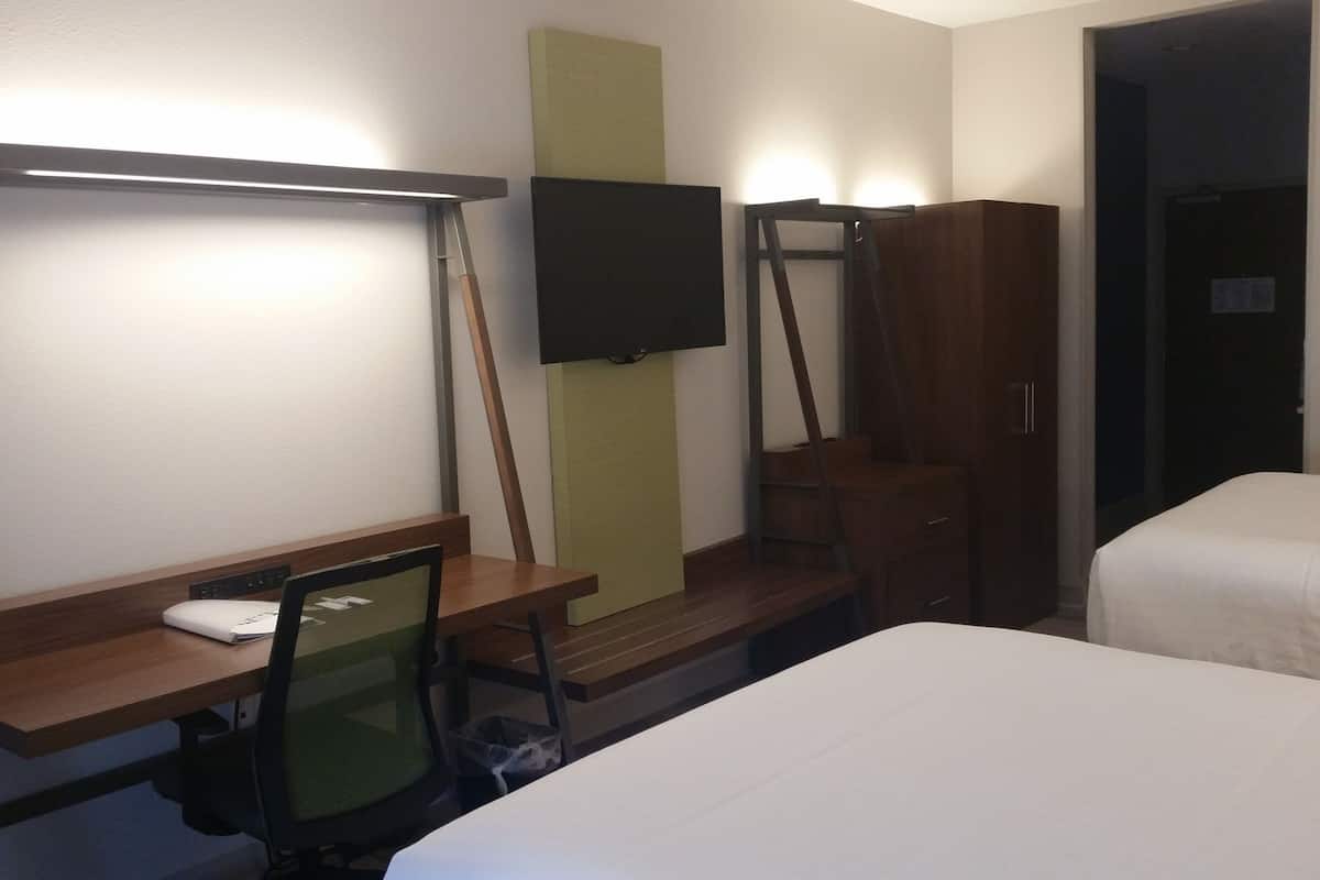 Hotellihuone, jossa on sänky, työpöytä tuolilla, seinälle asennettu televisio ja vaatekaappi.