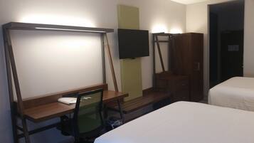 A hotel room with a bed, a desk with a chair, a television mounted on the wall, and a wardrobe.