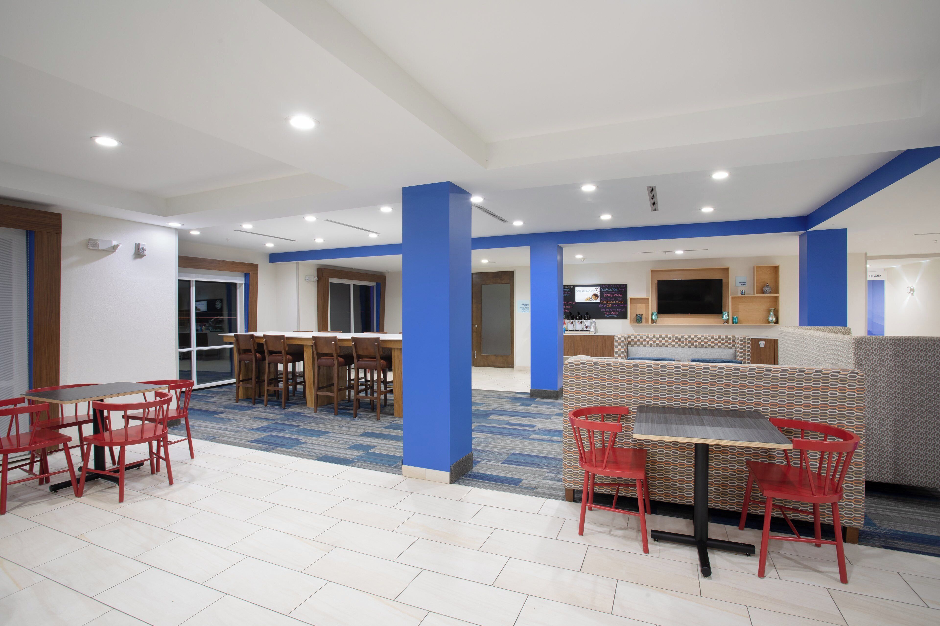 Un comedor moderno con techo alto, iluminación empotrada y diversos arreglos de asientos, incluyendo mesas y cabinas.