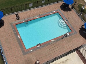 A rectangular swimming pool with a tiled deck surrounding it, a metal fence, and a sign indicating pool rules.