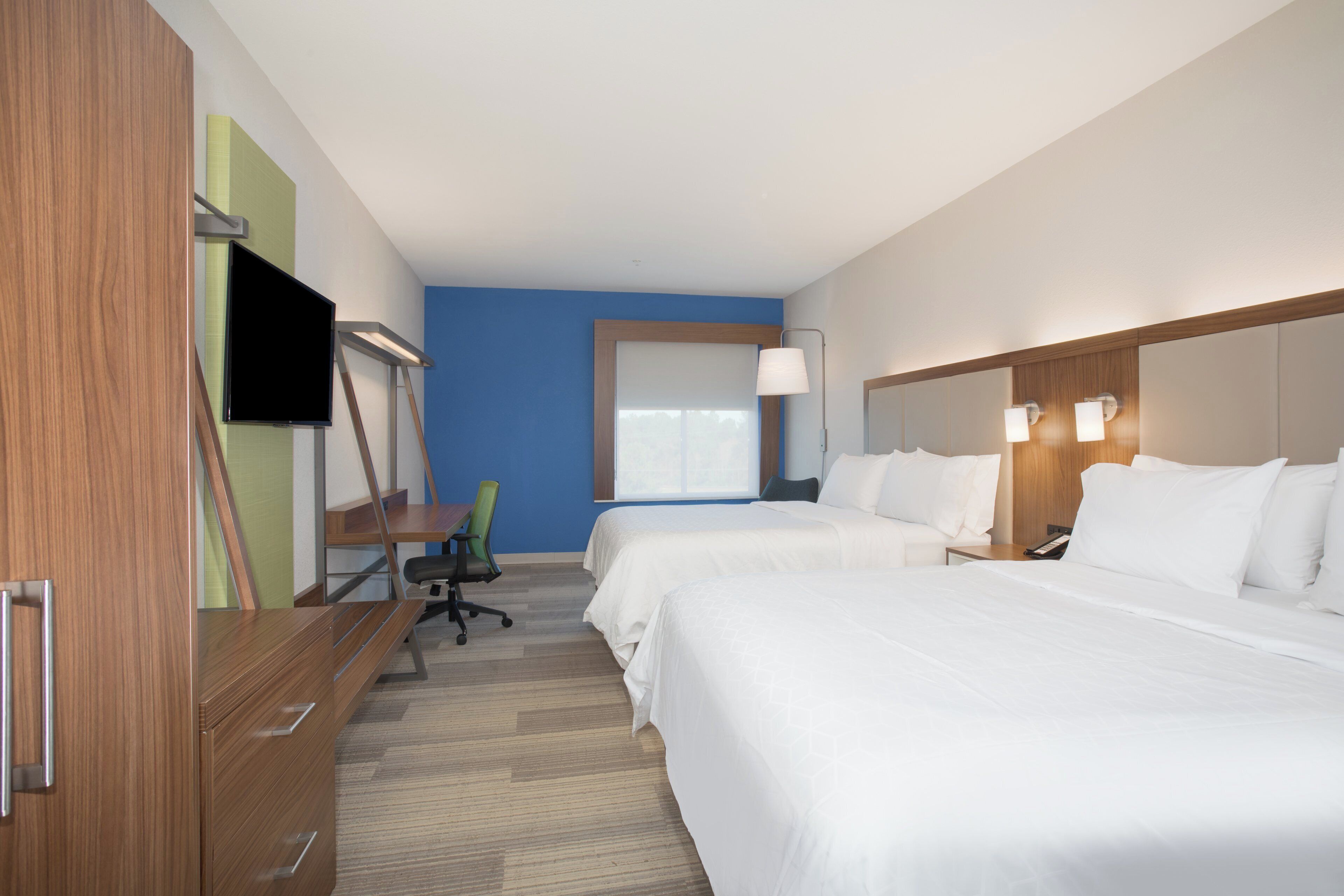 Una habitación de hotel con dos camas, un escritorio, una silla, un televisor y una ventana.