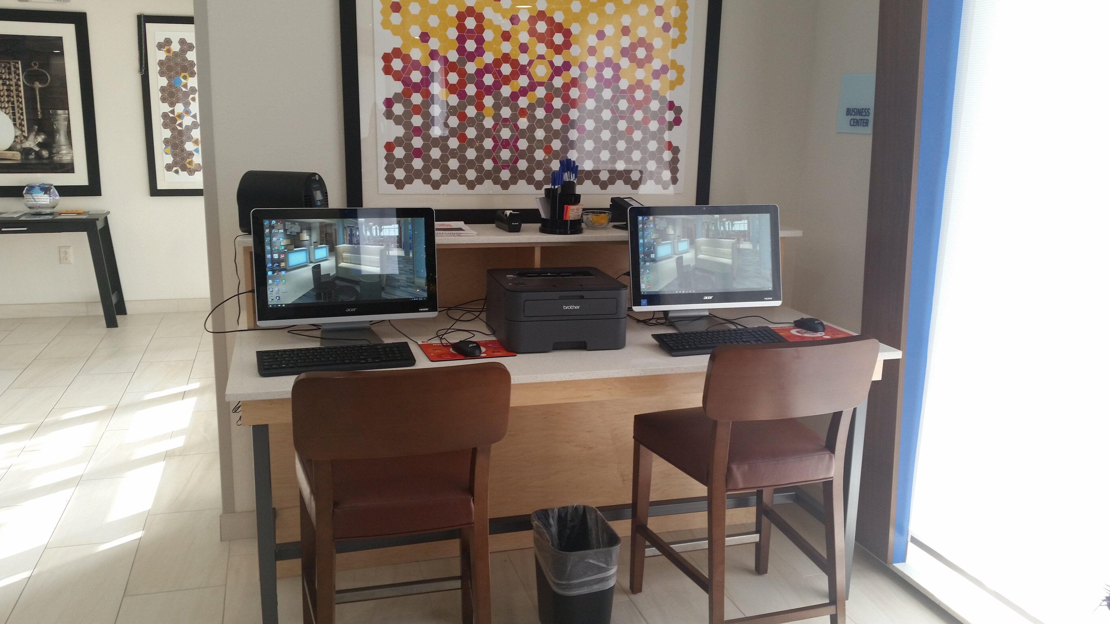 Un espacio de trabajo con dos monitores, una impresora y un cesto de basura.