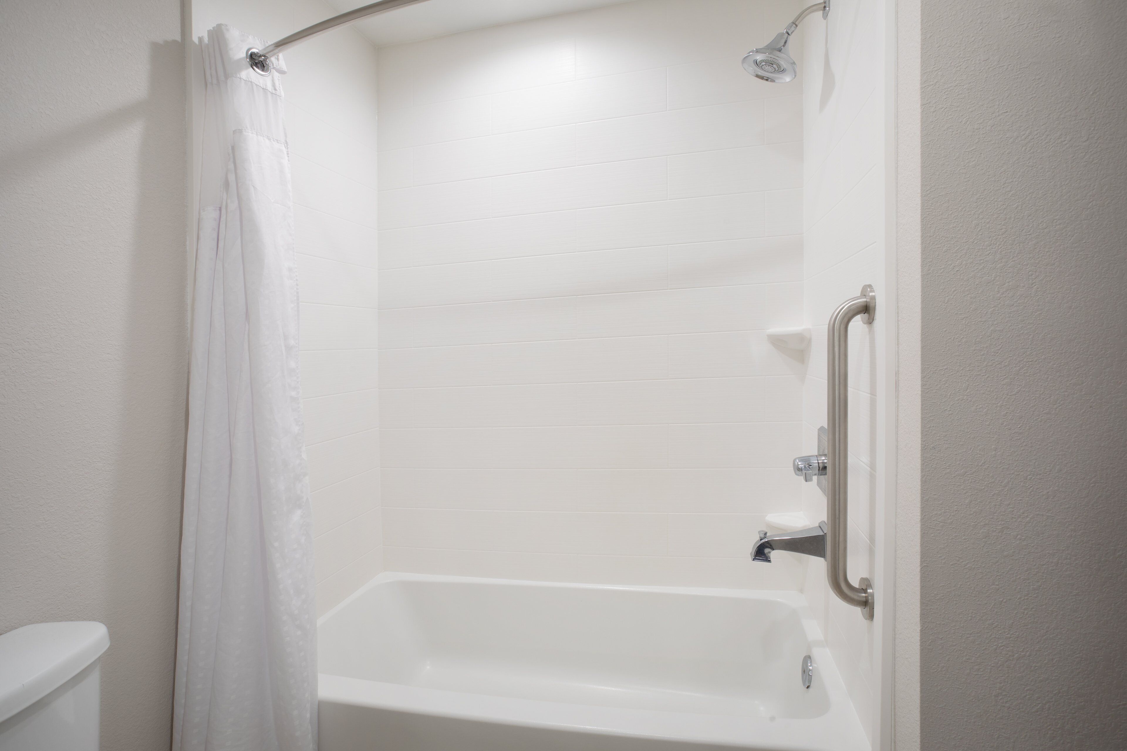 A bathroom with a white bathtub, a shower curtain, and a grab bar.
