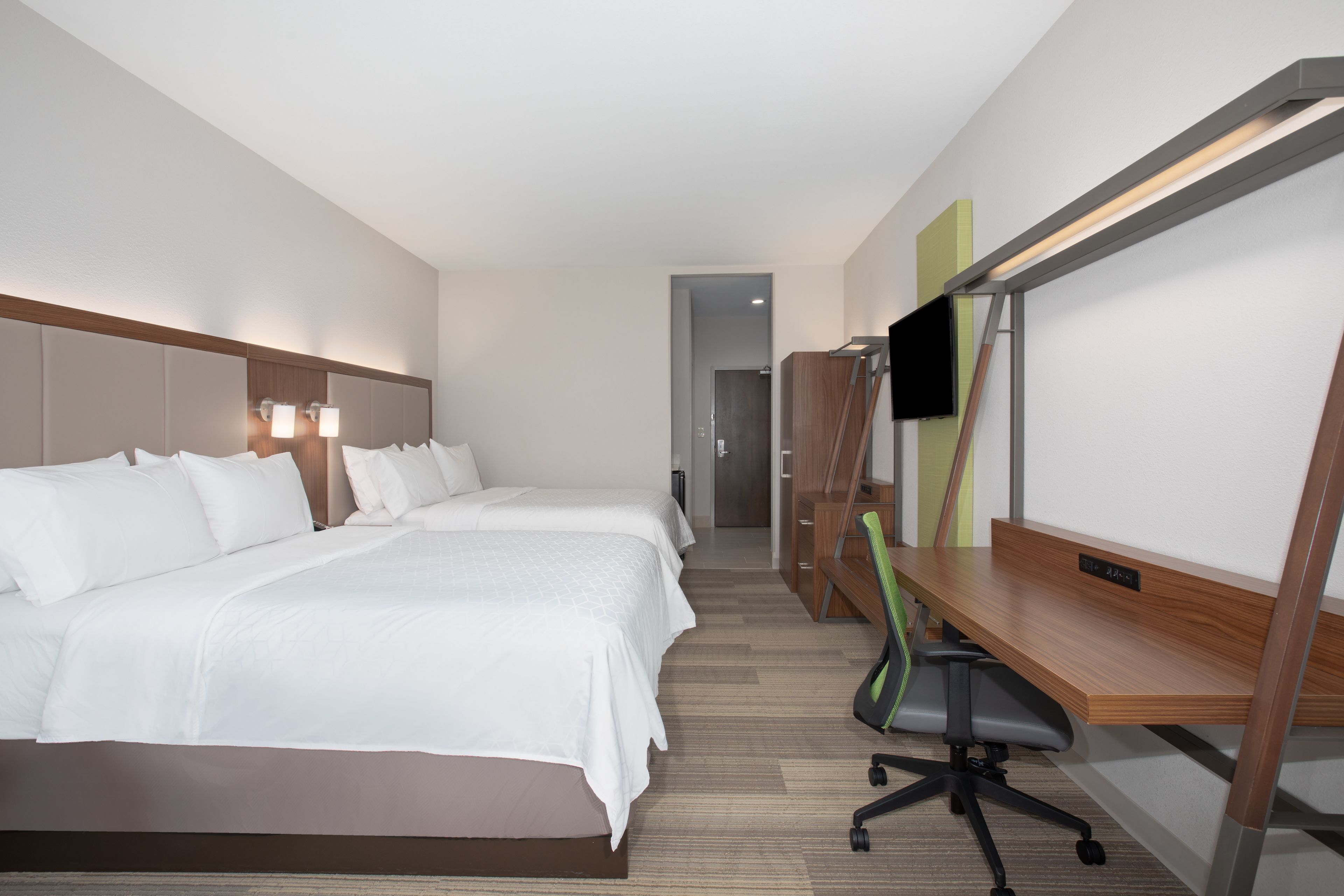 A hotel room with two beds, a desk, a chair, a flat-screen TV, and a wooden desk with a nameplate.