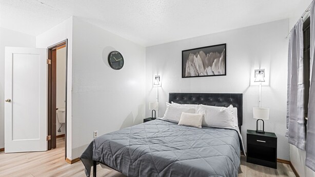 Une chambre à coucher avec un lit, deux tables de chevet avec des lampes, une horloge et un tableau encadré au mur.