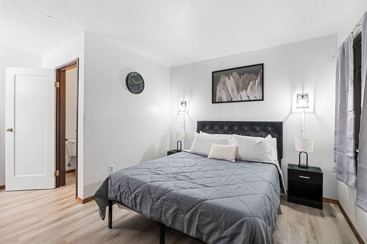 Un dormitorio con una cama, dos mesitas de noche con lámparas, un reloj y un cuadro en la pared.