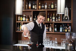 A bartender pouring a drink into a glass at a bar with shelves of liquor bottles in the background. - Constantine the Great (Belgrade)