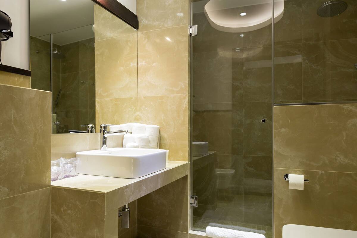 A modern bathroom with a large mirror, a sink, a bidet, a toilet, and a glass-enclosed shower area.